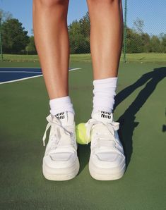 a person standing on a tennis court holding a tennis racket and ball in their shoes