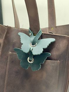 a brown leather bag with a green butterfly on the front and silver ring around the strap