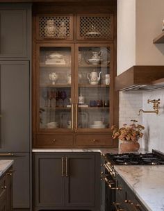 a kitchen with gray cabinets and white marble counter tops, gold trimming on the glass doors