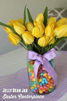 a glass jar filled with candy and yellow tulips next to a purple ribbon