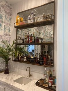 a kitchen sink sitting under a mirror next to a shelf filled with liquor bottles