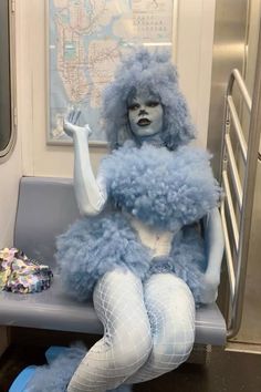 a woman dressed in blue and white sitting on a subway train seat with her legs crossed