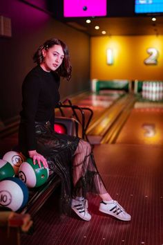 a woman sitting on top of a bench next to bowling balls in a bowling alley