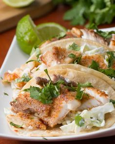 three fish tacos on a white plate with limes