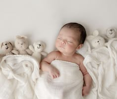 a baby is sleeping with stuffed animals in the background on a white blanket that has been draped over