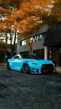 a blue sports car parked in front of a building next to trees with orange leaves