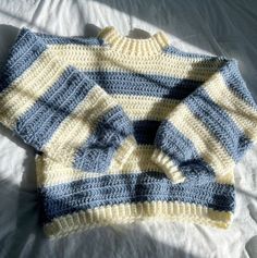 two knitted sweaters sitting on top of a bed next to each other in blue and yellow