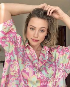 a woman in a pink floral shirt is holding her hair up and looking at the camera