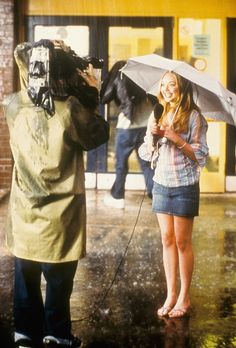 a woman holding an umbrella while standing next to a man with a camera on a rainy day