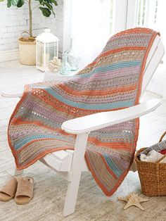 a crocheted blanket sitting on top of a white chair next to a basket