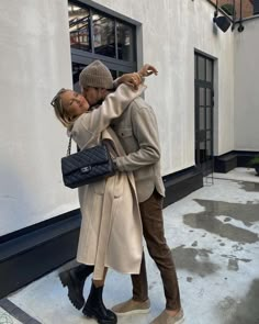 a man and woman are kissing in front of a building with snow on the ground