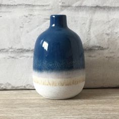 a blue vase sitting on top of a wooden table next to a white brick wall