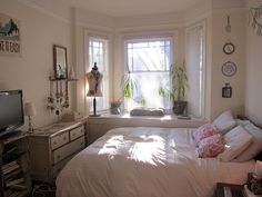 a bedroom with a bed, dresser and television in the corner next to two windows