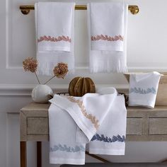 two white towels hanging on the wall next to a vase with dried flowers in it