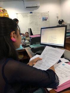 a woman sitting at a desk in front of a computer with papers on her lap