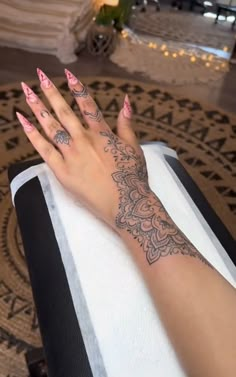 a woman's hand with tattoos on her left arm and pink manicures