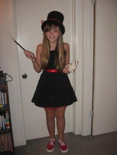 a girl in a black dress and top hat holding a wand while standing next to a door