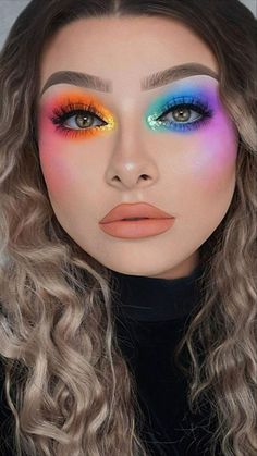 a woman with long curly hair and bright makeup looks at the camera while wearing colorful eyeliners