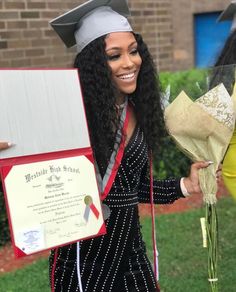 a woman in graduation gown holding flowers and a plaque