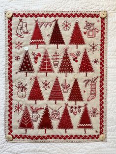 a red and white quilted wall hanging with christmas tree designs on it's side