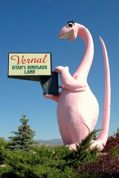 a large pink dinosaur statue holding a sign