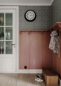 a clock on the wall above a door in a room with pink walls and wooden flooring