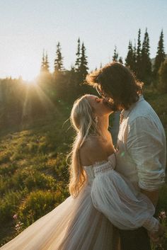 a bride and groom kissing in the mountains at their wedding day, with the sun shining through the trees behind them