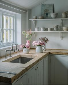 a kitchen with white cabinets and pink flowers in vases on the sink counter top