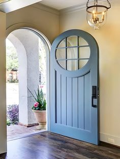 a blue front door with an arched glass window and potted plant on the side