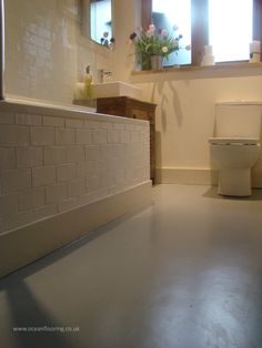 a white toilet sitting next to a bath tub in a bathroom under a window with flowers on the ledge