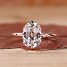 an oval cut diamond ring sitting on top of a leaf