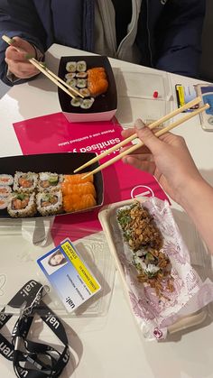 two people eating sushi with chopsticks at a table in front of them