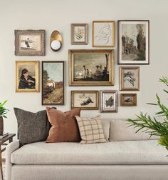 a living room filled with lots of framed pictures and paintings on the wall next to a couch