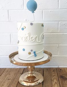 a white and blue birthday cake on a gold stand with a balloon in the air