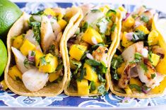 fish tacos with mango salsa on a blue and white plate next to limes