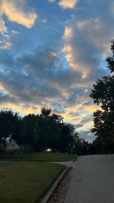 the sky is filled with clouds and some trees in front of a road that has grass on both sides