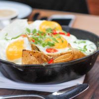 a black bowl filled with food on top of a wooden table next to silverware