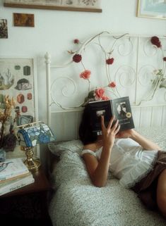 a woman laying in bed reading a book with her hand up to her face while holding an electronic device