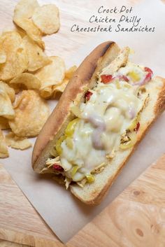 a close up of a hot dog with cheese and toppings next to potato chips