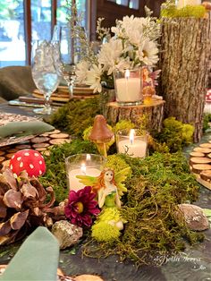 the table is set with candles, moss and fairy figurines