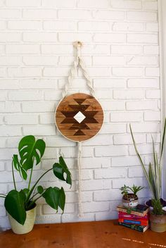 a wooden sign hanging from the side of a white brick wall next to potted plants