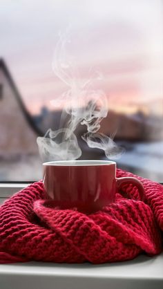 a cup of coffee with steam rising out of it sitting on a window sill