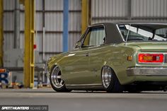 an old green car parked in front of a warehouse building with it's hood up