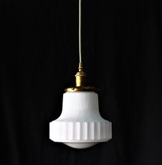 a white light hanging from a gold colored metal fixture on a black background with a cord