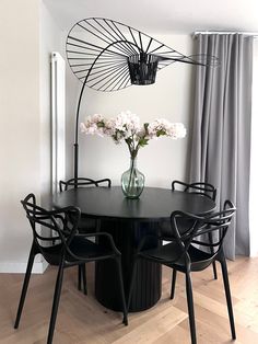 a black table with four chairs around it and a vase filled with flowers on top