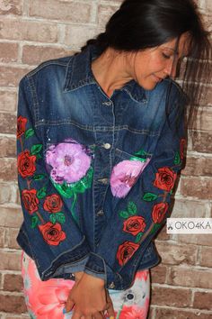 a woman wearing a jean jacket with flowers painted on the front and back, standing in front of a brick wall