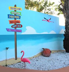 a pink flamingo standing in front of a blue wall with directional signs on it