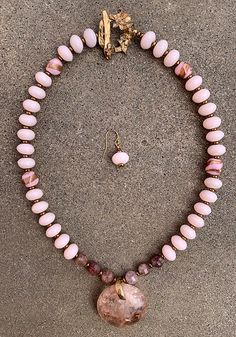 a necklace and earring set with pink beads on concrete ground next to small gold plated object