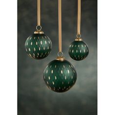 three green and gold ornaments hanging from brass hooks on a black background with white dots