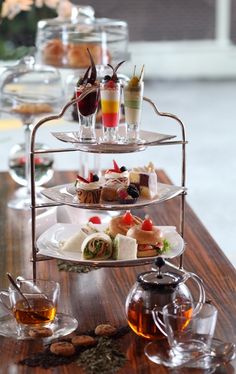 three tiered trays filled with different types of desserts and drinks on top of a wooden table